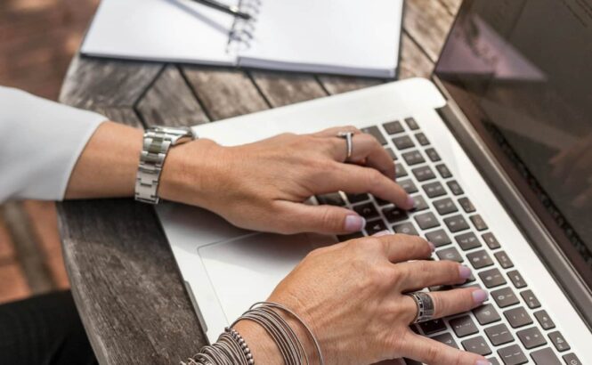 A person working at a table with a laptop. There is a pen and notebook to the side.