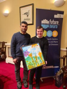 Two young males standing in front of the FutureNeuro pull-up banner, holding one of the winning entries of our art competition.