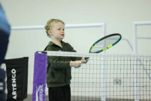 A young boy with blonde hair holding a tennis racket.