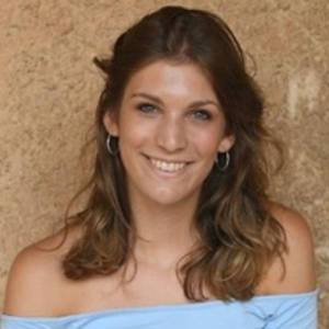 Headshot of a girl with brown hair, tanned skin, wearing a light blue top.