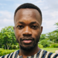 Head-and-shoulders portrait of a person wearing a patterned top, photographed outdoors with trees and sky softly blurred behind.
