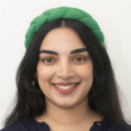 Head‑and‑shoulders studio portrait of a person with long dark hair wearing a braided green headband and a dark top, photographed against a plain light background.