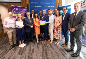 A group of attendees pose for a photo at a healthcare advocacy event in front of Neurological Alliance of Ireland, European Union, and patient organisation banners. Several participants hold declarations while standing alongside colleagues and stakeholders. The group is gathered in a conference setting with Irish and EU branding visible in the background, marking the presentation of declarations supporting improved neurological care and health policy initiatives.