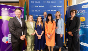 A group of representatives from healthcare, research, and patient advocacy organisations pose for a photograph at a Neurological Alliance of Ireland event. The group stands between Neurological Alliance of Ireland and FutureNeuro banners, with Irish and EU flags and an Ireland-EU backdrop displayed behind them. The photo was taken in a conference setting and highlights collaboration between stakeholders working to advance neurological research, innovation, and patient care in Ireland.